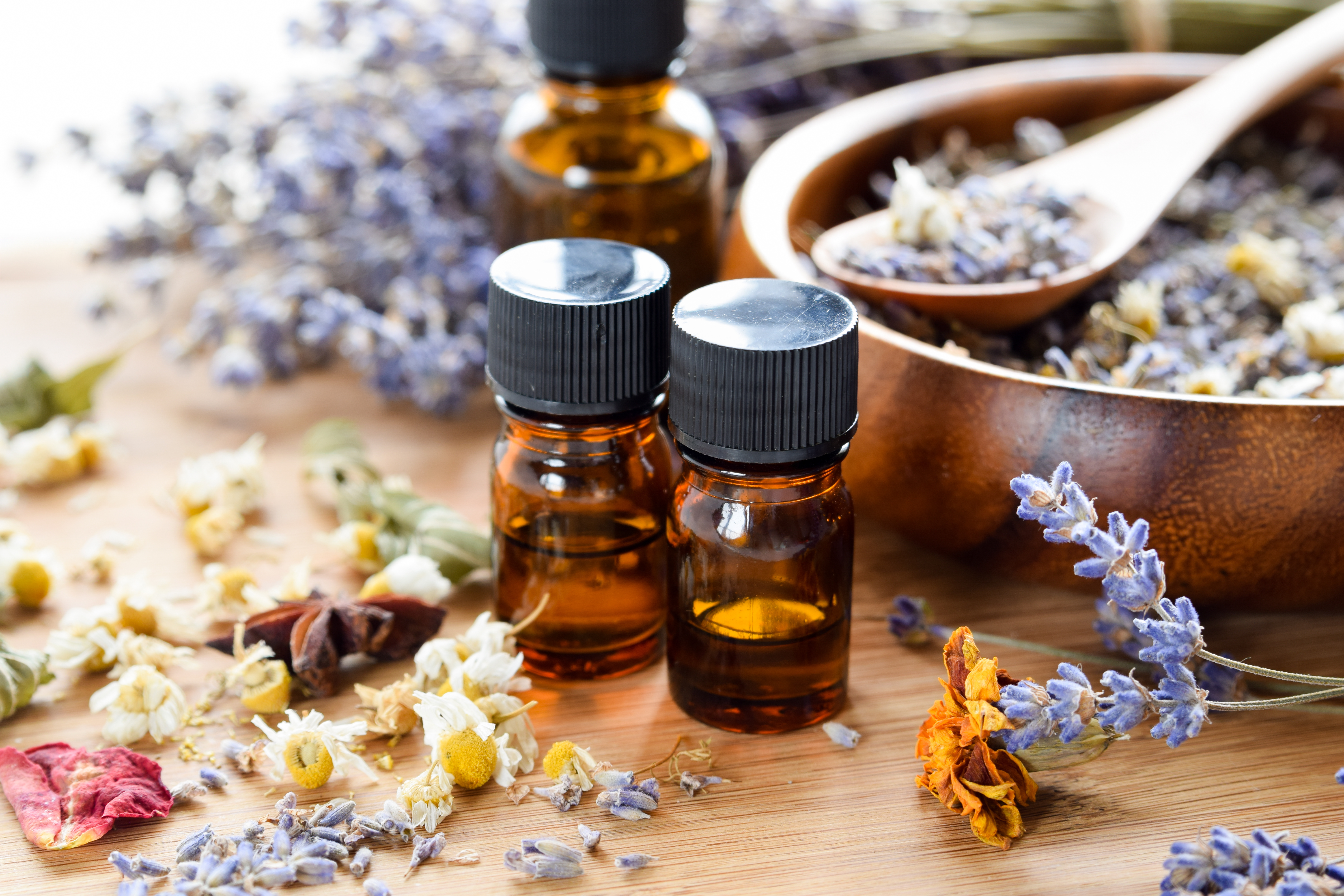 3 small brown bottles with essential oils inside. Small bowl of flowers behind.