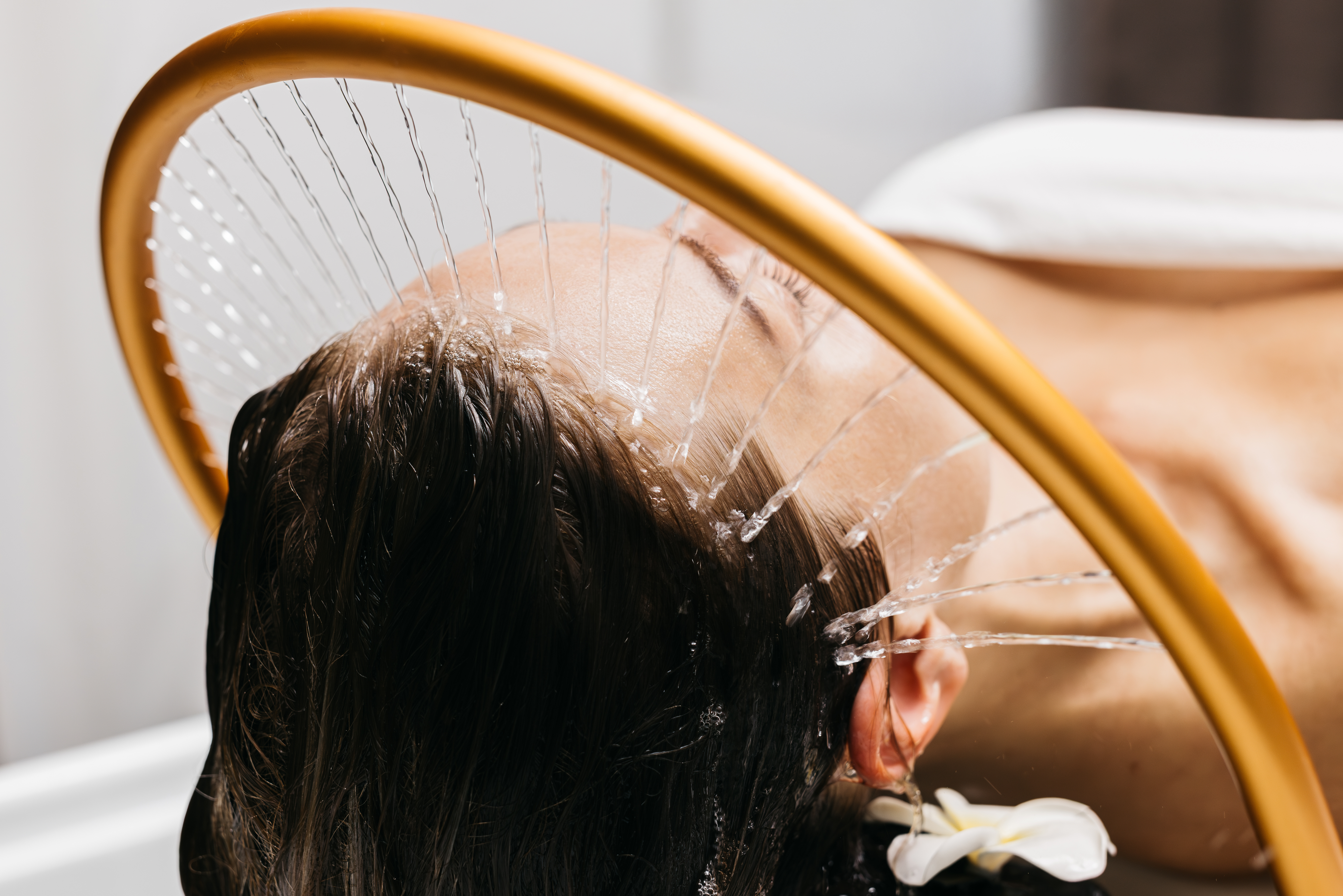 Woman lying on massage table, a circular water nozzle spraying water at her scalp