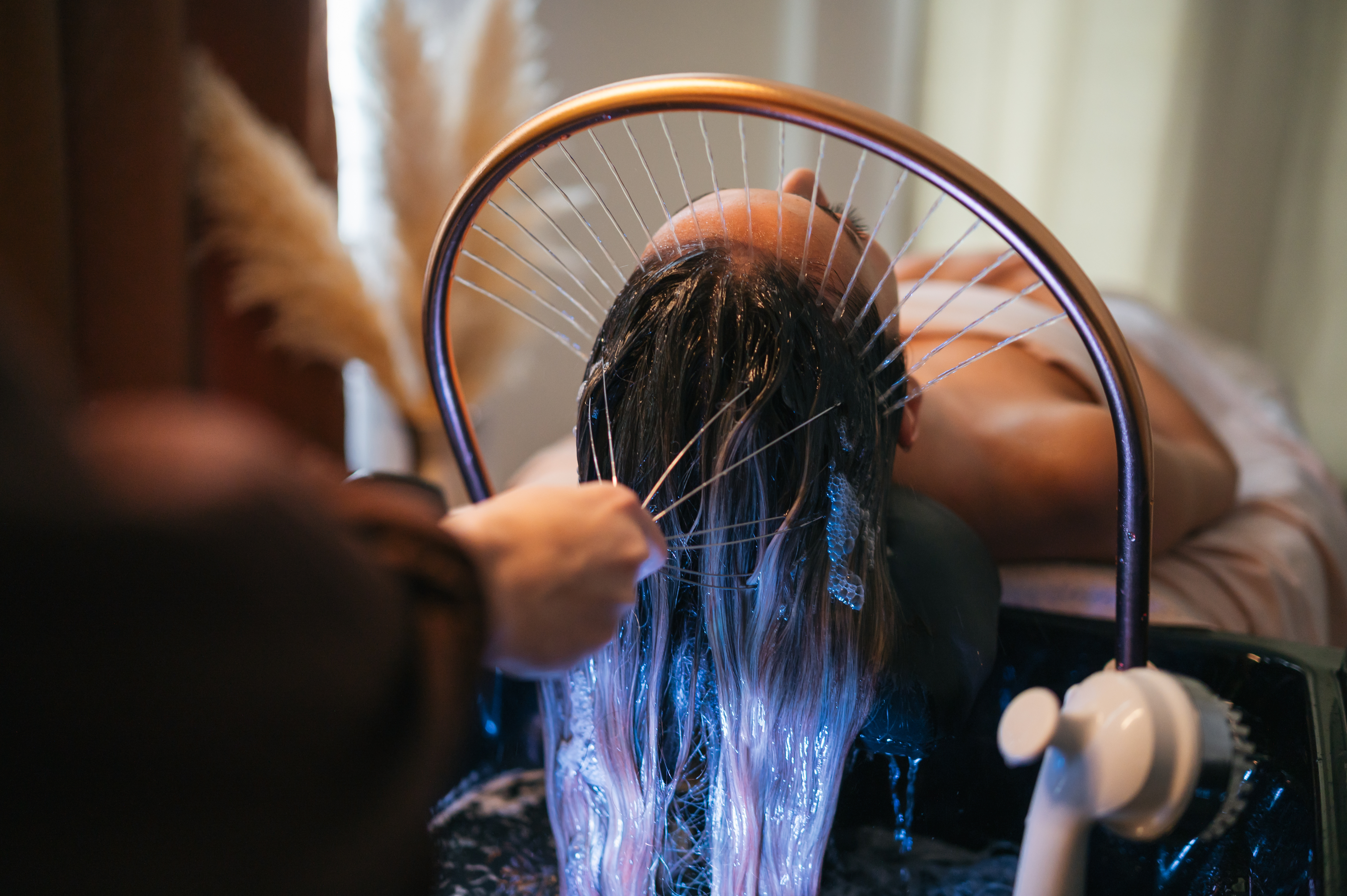 woman laying on massage table with water being sprayed on her, and a clinician is rubbing her scalp with a massage device 